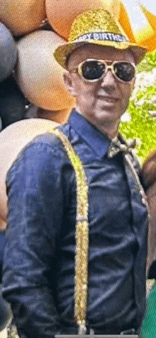 a man wearing a hat that says happy birthday is standing in front of balloons