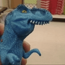 a person is holding a blue dinosaur toy with a very large mouth .