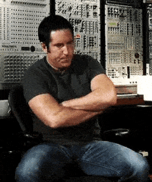 a man is sitting in a chair with his arms crossed in front of a wall of electronic equipment .