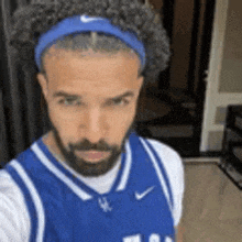 a man with a beard is wearing a blue basketball jersey and a headband .