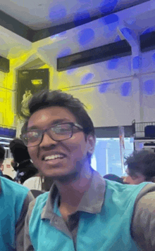 a man wearing glasses and a blue shirt smiles in a crowded room