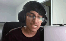 a young man wearing headphones and glasses looks at a laptop