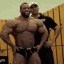 two men are posing for a picture in a locker room . one of the men is very muscular .