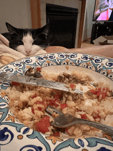 a black and white cat is looking at a plate of food with a knife and fork