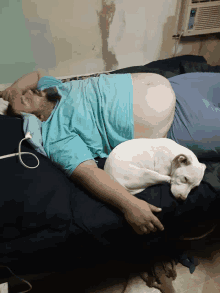 a man is laying on a bed with a white dog on top