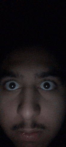 a close up of a man 's face with his eyes wide open in the dark