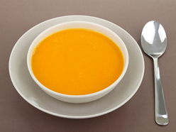 A bowl of carrot soup on the table with a spoon next to it