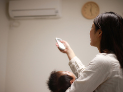 Woman holding a baby and pointing a remote towards an air conditioner