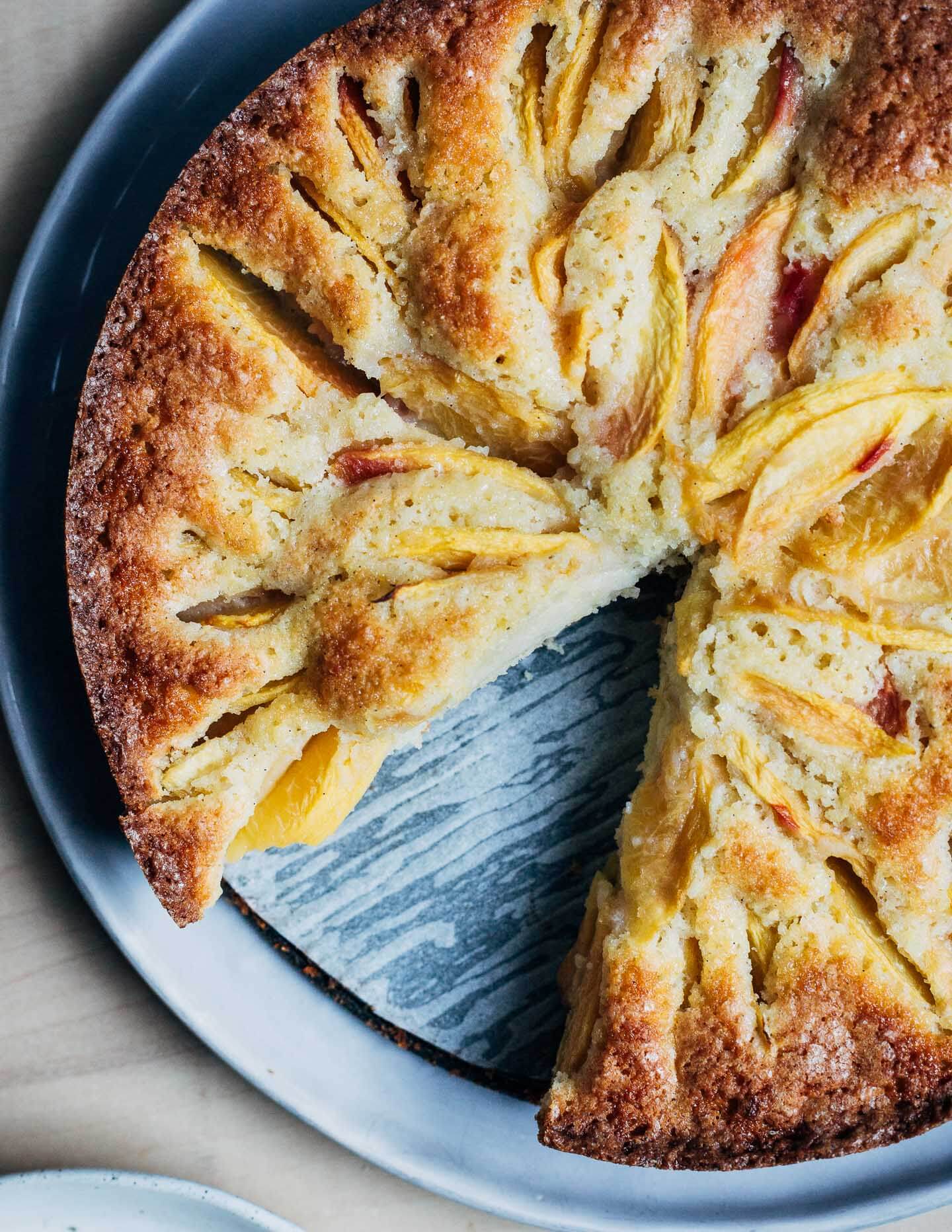 A peach-studded cake on a platter with one slice taken out. 