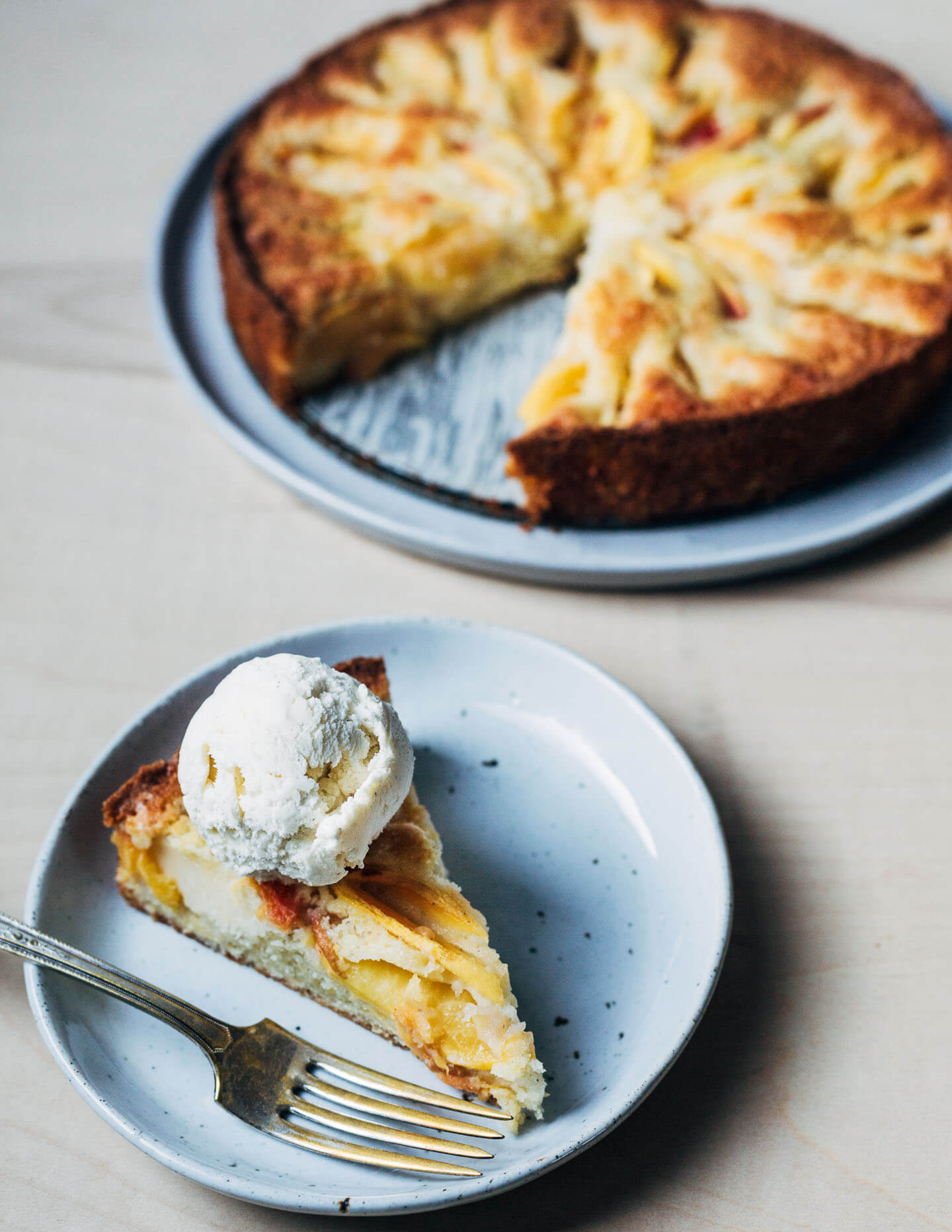 A peach cake with a slice removed and a slice alongside with a scoop of ice cream on top. 