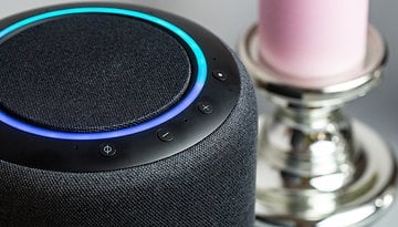 Nahaufnahme eines Smart Speakers mit blauer Ringbeleuchtung und Steuerungen, neben einer rosa Kerze.