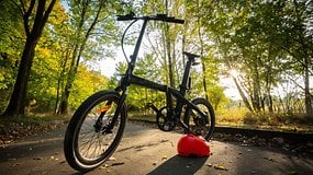 Ein schwarzes Fahrrad mit dünnen Reifen und einem roten Helm, der auf einem Weg umgeben von Bäumen im Herbst ruht.