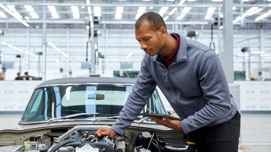 A car engineer is checking the parts of a car with its hood open and he is holding an ASUS ExpertBook B3 detachable laptop.