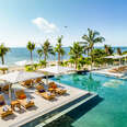 a shot of the beach from the pool of a resort, with coconut trees 