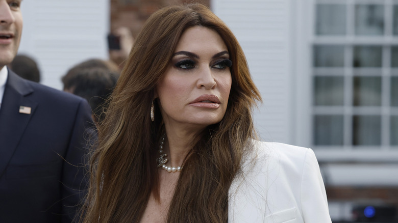 Kimberly Guilfoyle looking sad while wearing a white jacket in front of the White House