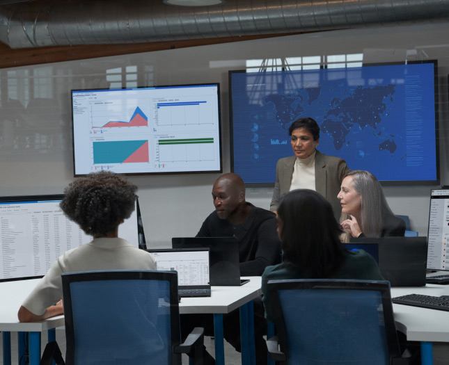 Five people having a meeting in a conference room with their laptops and additional monitors