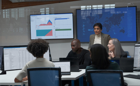 Five people having a meeting in a conference room with their laptops and additional monitors