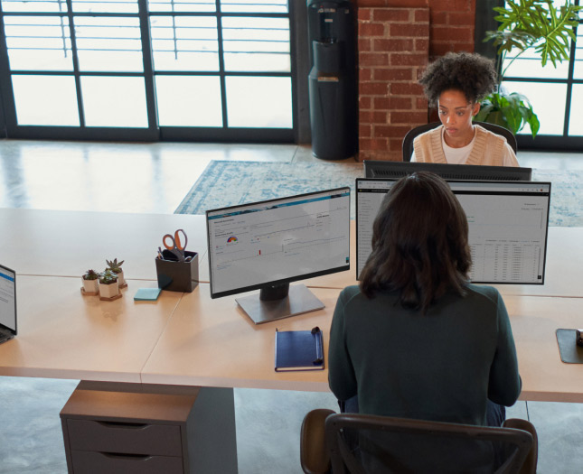 Two women working on their laptops in front of each other at the office