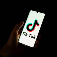 This photograph taken on April 19, 2024 shows a man holding a smartphone displaying the logo of Chinese social media platform Tiktok in an office in Paris