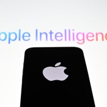 the 'Apple' logo is displayed on a mobile phone screen in front of a computer screen displaying Apple Intelligence logo