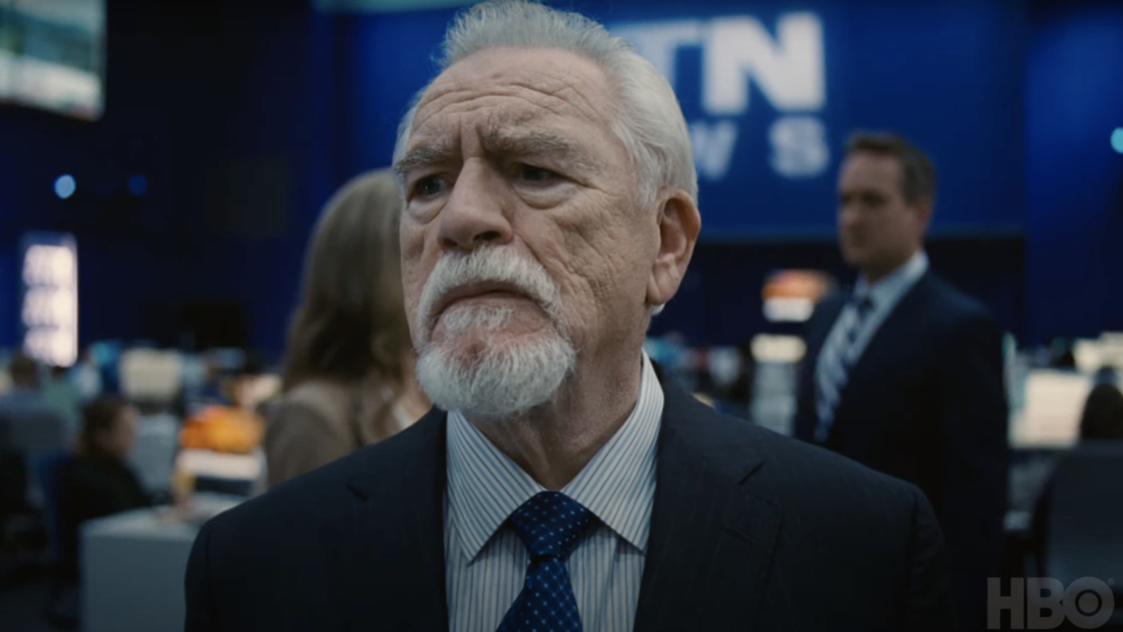 An older man in a suit stands in the main floor of a media company.