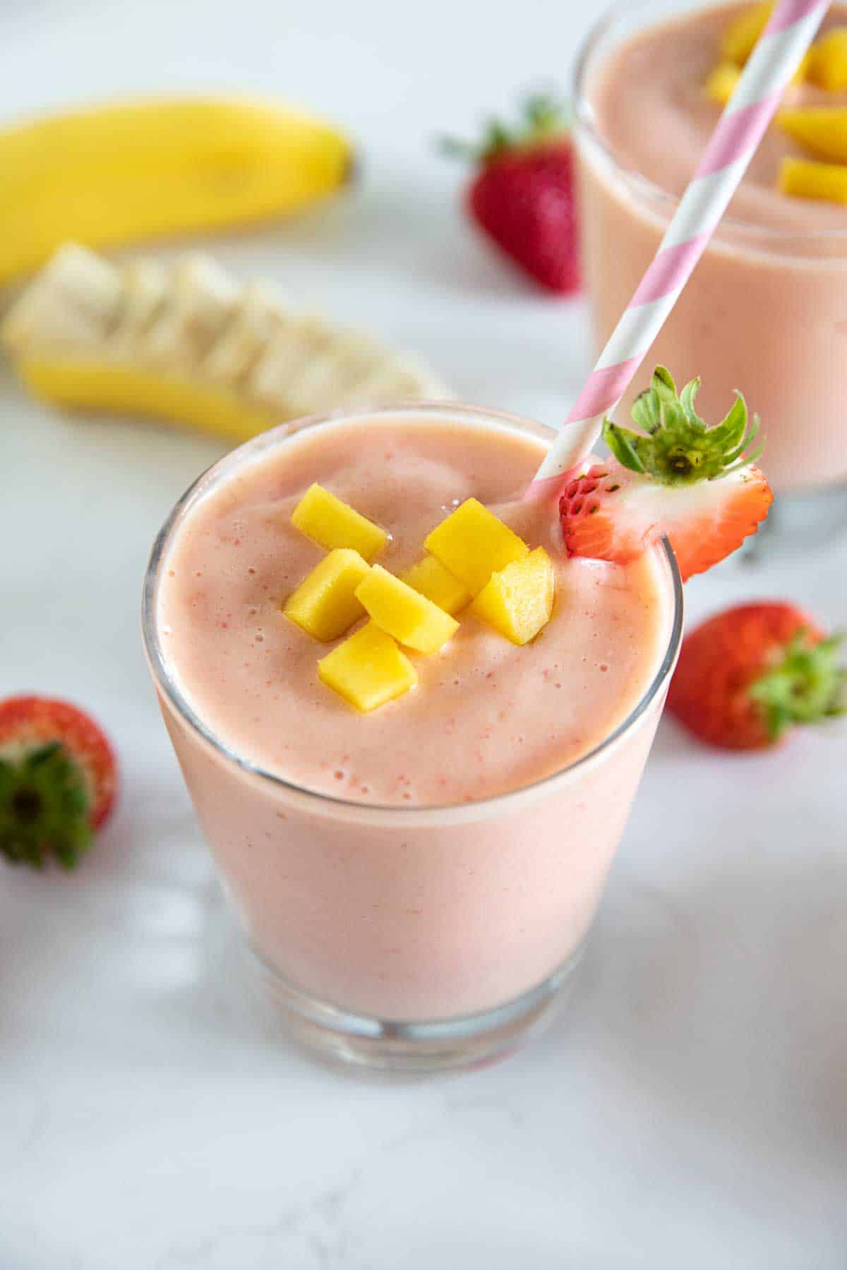 cup of tropical smoothie with a straw topped with mango and strawberry