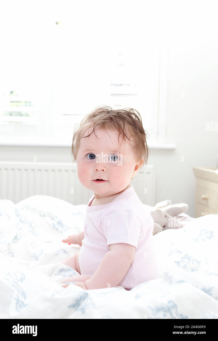 Baby sat in bed looking at camera Stock Photo