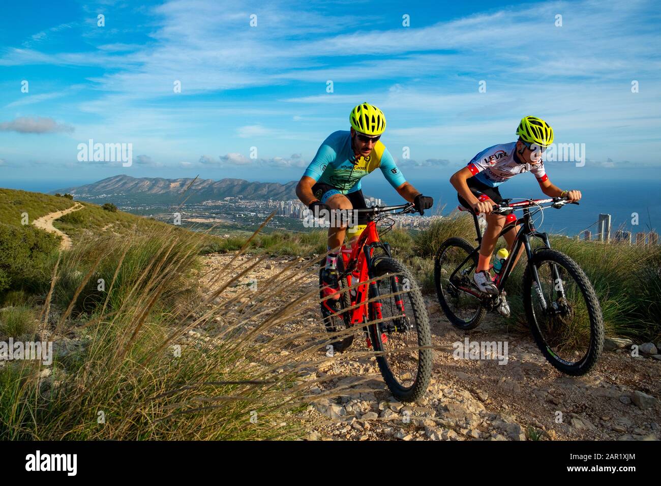 Two mountain bikers riding on hill with Benidorm city in the background, Sierra Cortina, Benidorm, Alicante province, Spain Stock Photo