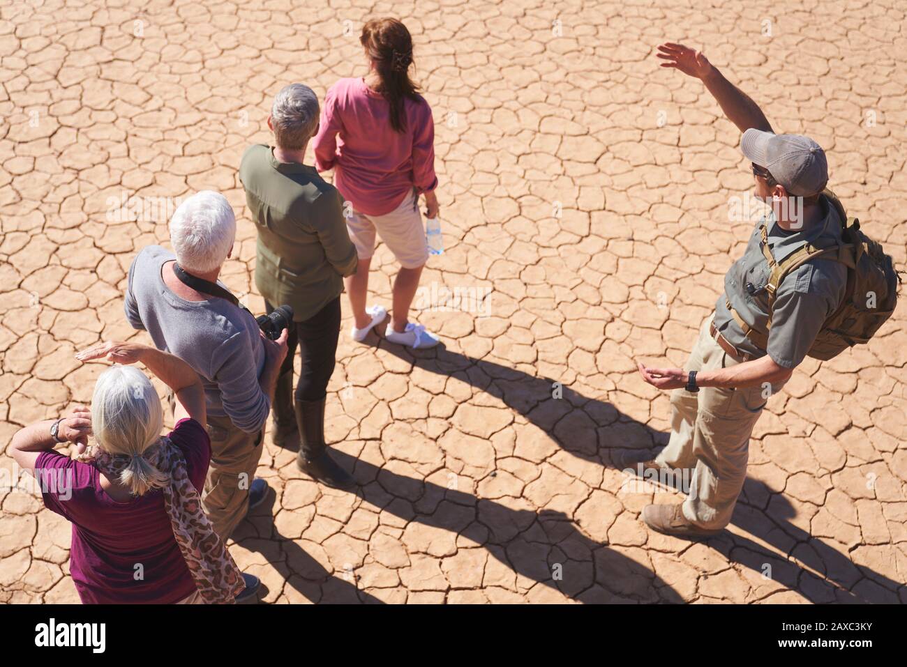 Safari tour guide talking with group on sunny cracked earth Stock Photo