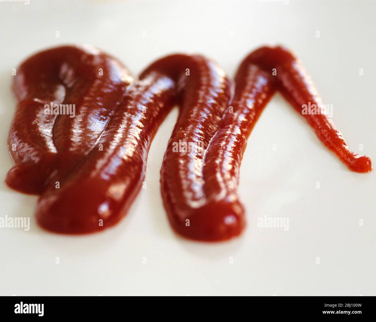 Squiggle of tomato ketchup squeezed out of squeezy bottle on white background. SHort depth of field. - Stock Photo