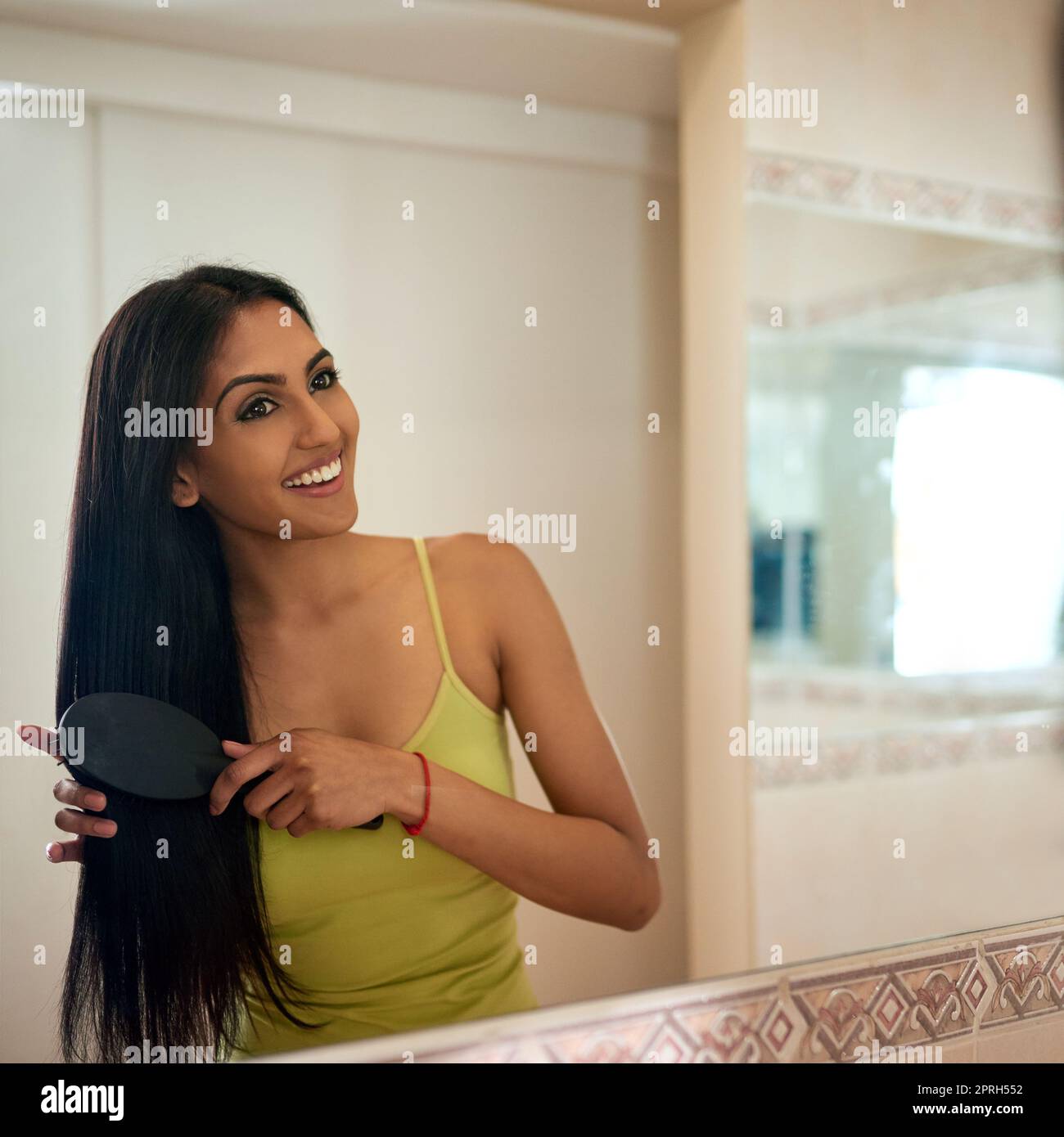 Maintaining her sleek and smooth hair. a young woman brushing her hair in the bathroom. Stock Photo