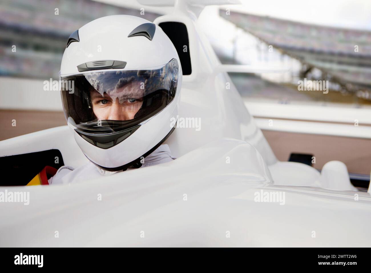 A focused individual clad in a white racing helmet sits in the cockpit of a sleek racecar. Stock Photo