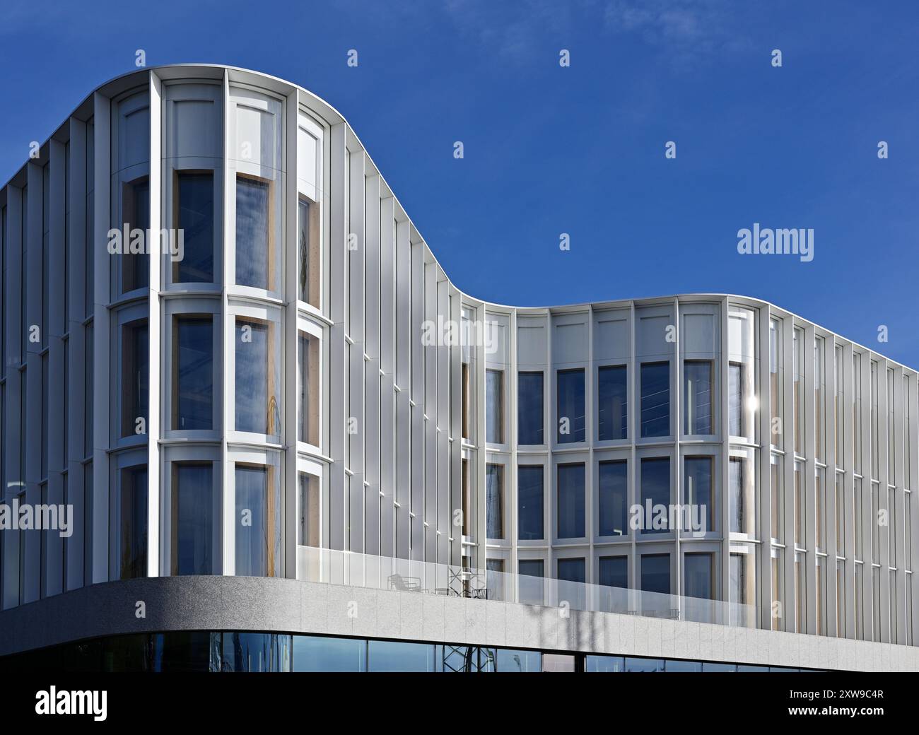 The image showcases a modern architectural building with a sleek and wavy façade. The structure features large, vertically aligned windows framed by a Stock Photo