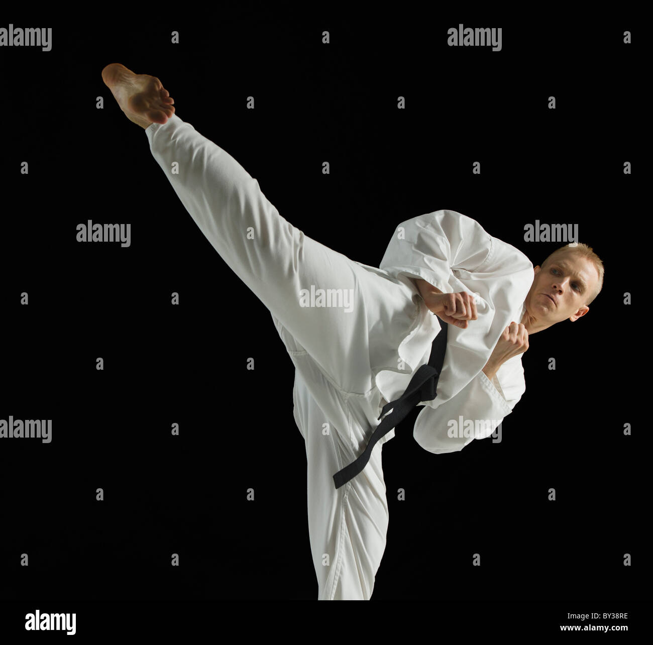 Young man performing karate kick on black background Stock Photo