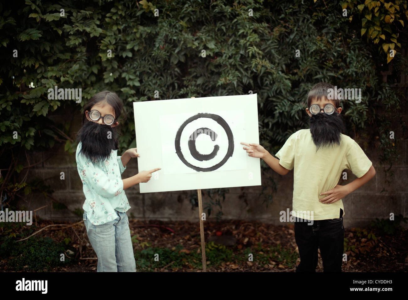 Boy and girl dressed up with fake beards point to copyright symbol. Stock Photo