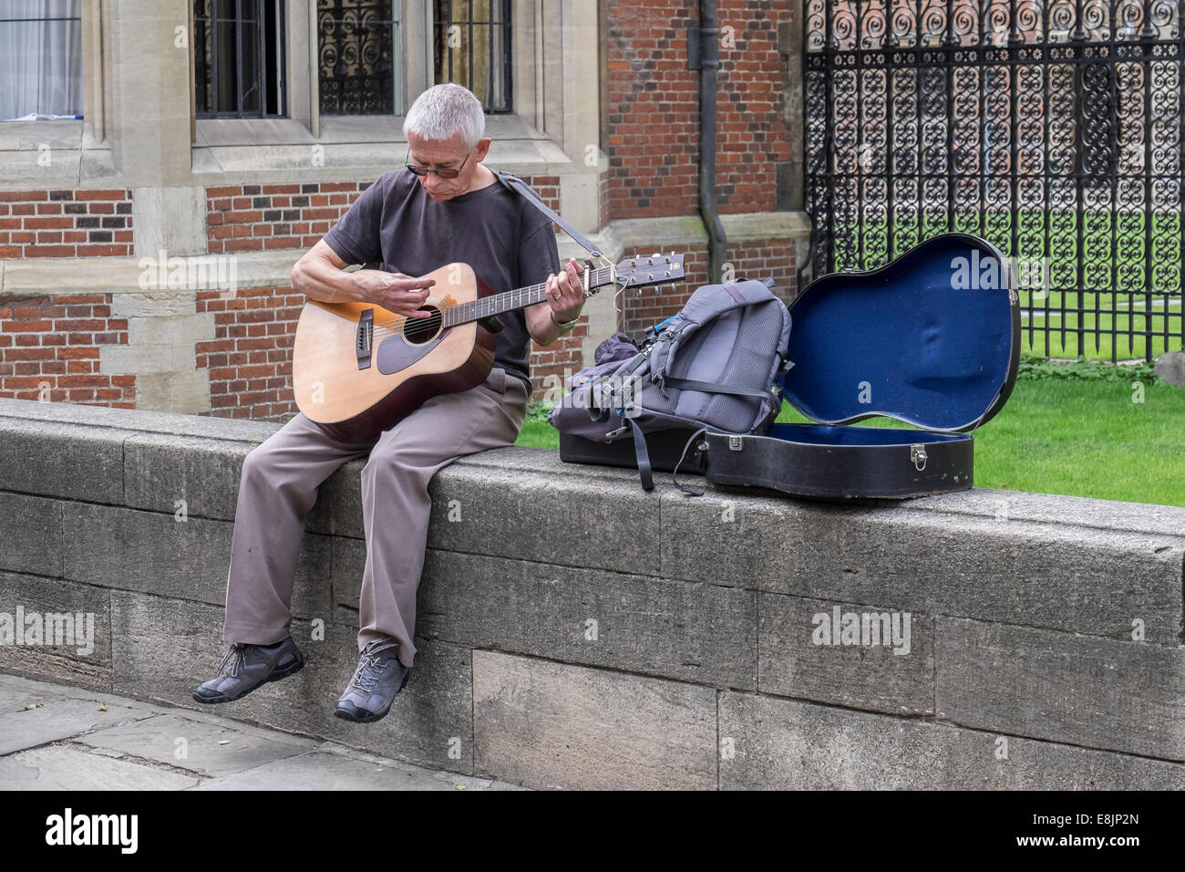 Man busking on guitar sat on wall St Johns college Cambridge Cambridgeshire England Stock Photo