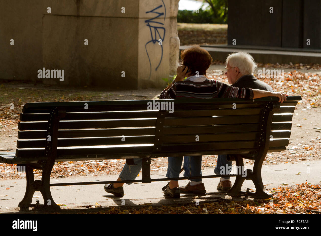 couple sat on bench graffiti tourists sun on phone Stock Photo