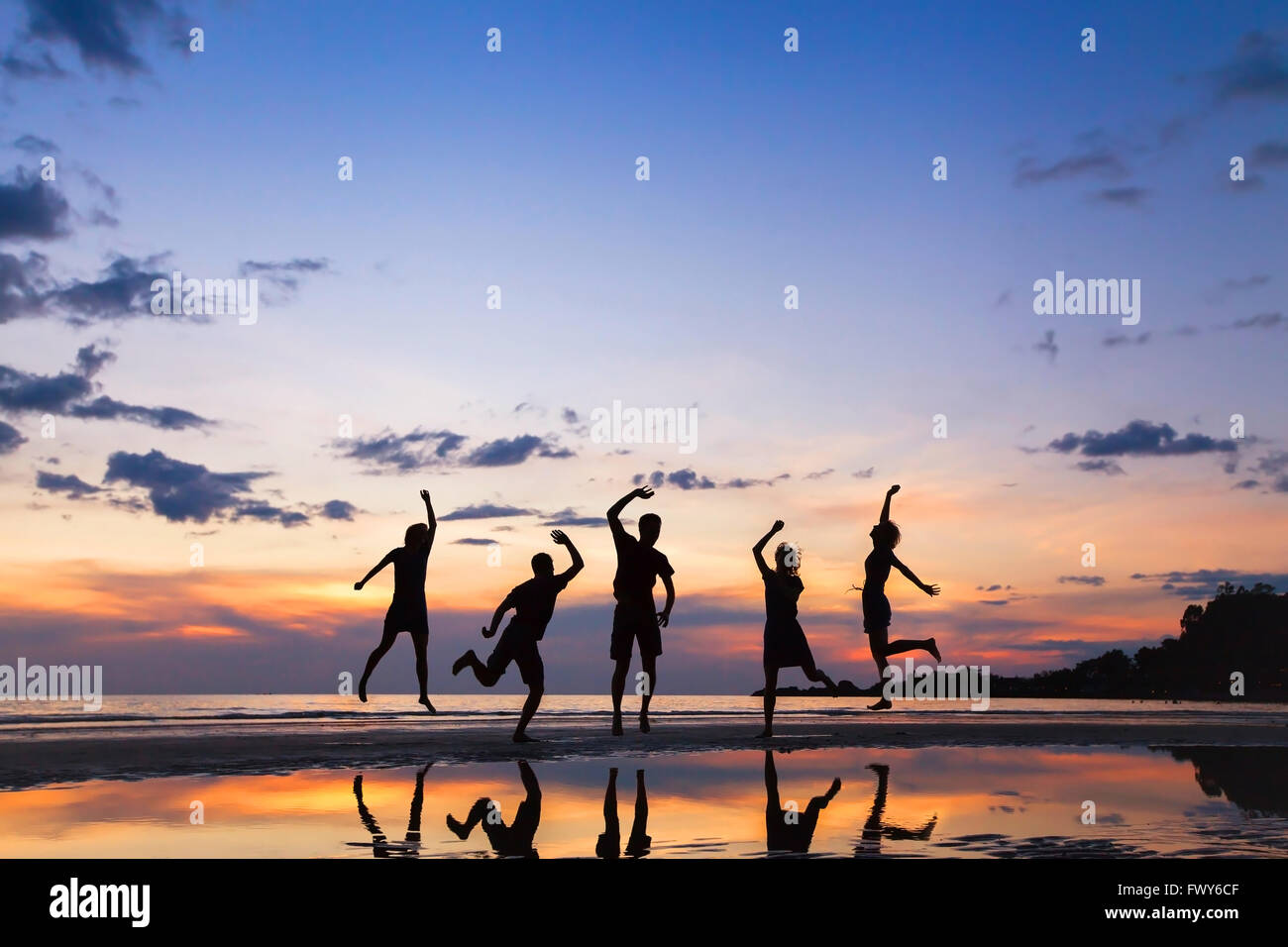 group of people jumping on the beach at sunset, silhouette of friends having fun together Stock Photo