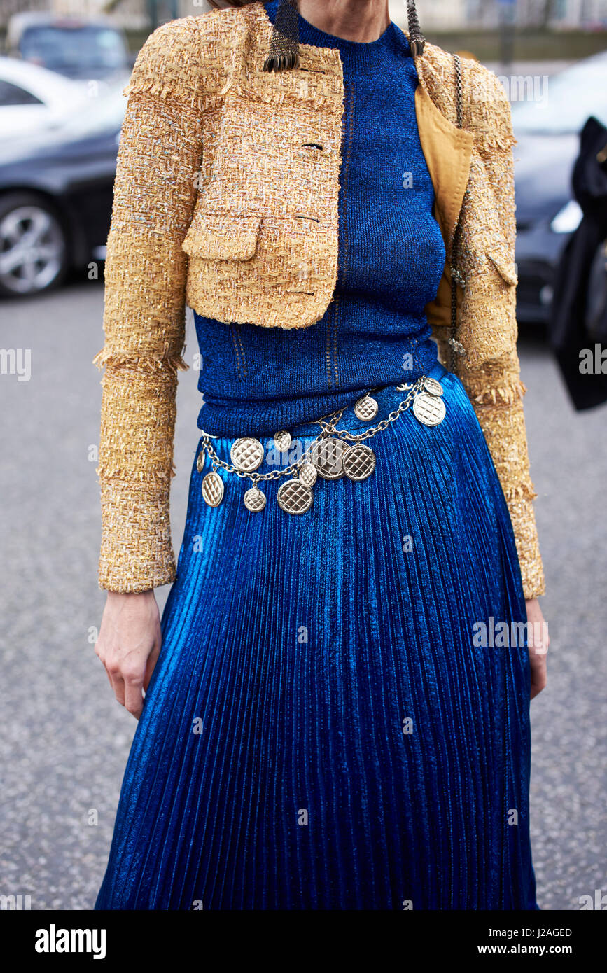 LONDON - FEBRUARY, 2017: Mid section of woman wearing a short wool jacket, long blue pleated skirt and a Chanel medallion chain belt in the street during London Fashion Week, vertical, front view Stock Photo