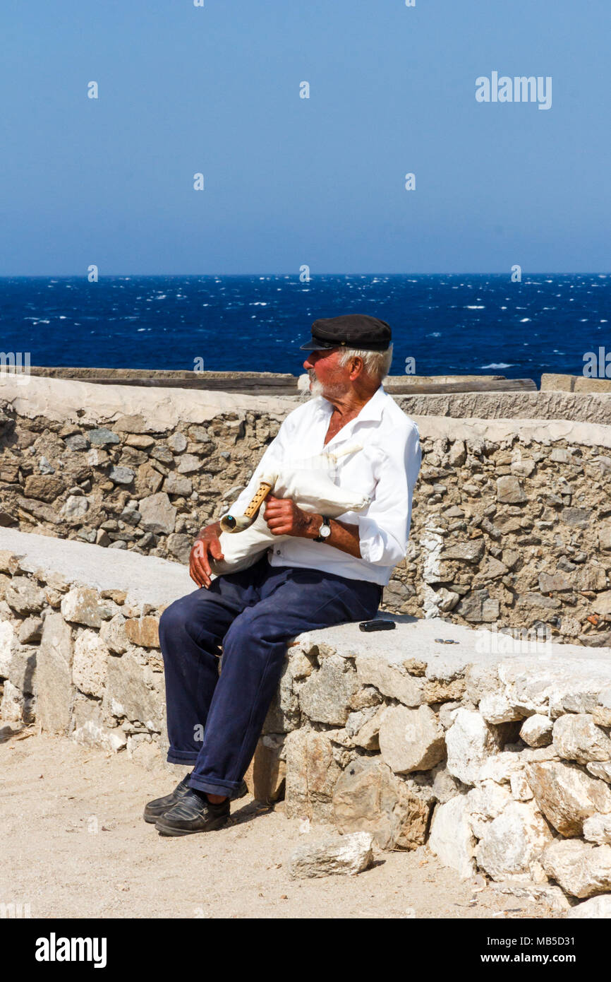 Old man sat on wall with bagpipe, Mykonos, Greece Stock Photo