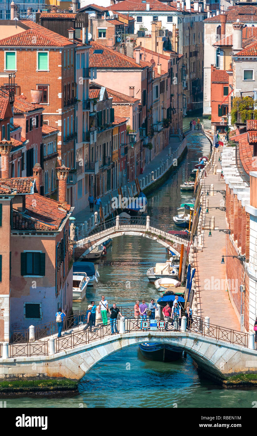 High aspect view of small canal with houses either side, bridge, boats and tourists standing on bridge Venice, Venezia, Veneto, Italy, Europe Stock Photo