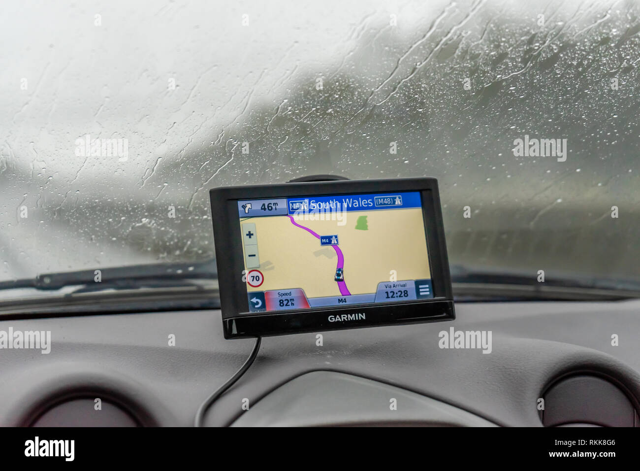 A Garmin sat nav or satellite navigation / satnav system mounted to a car wind screen during rainy weather driving in Wales, UK, Europe Stock Photo