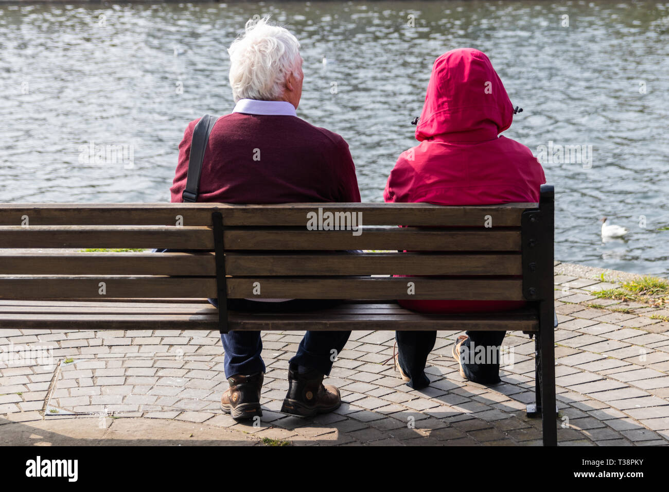 Elderly couple sat on a wooden bench overlooking the water Stock Photo