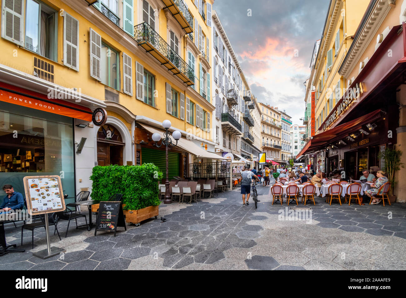 Ein Mann sein Fahrrad Vergangenheit Straßencafés in der Dämmerung im touristischen Zentrum von Nizza, Frankreich, an der Französischen Riviera. Stockfoto