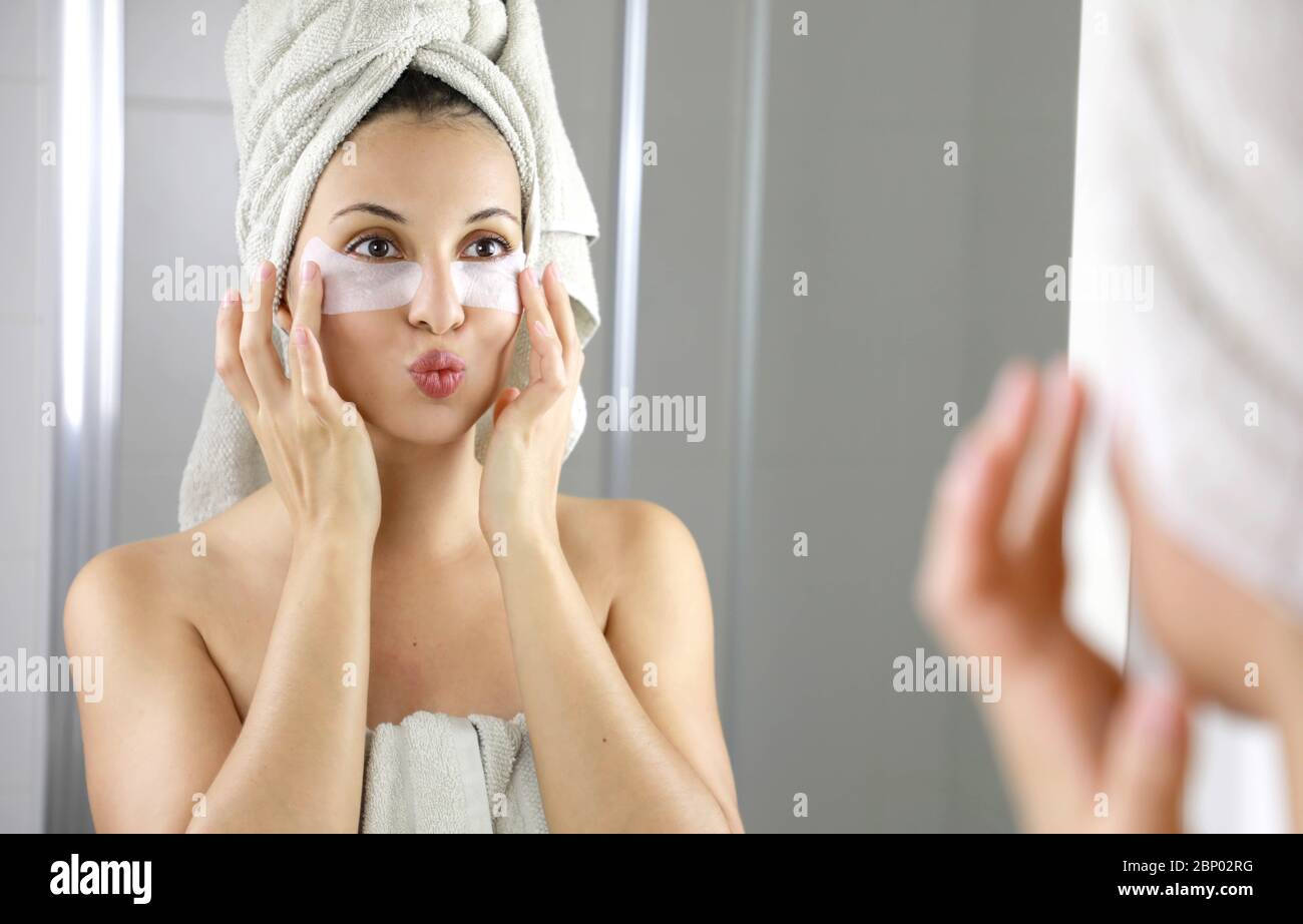 Schöne Frau Anwendung Anti-Müdigkeit unter den Augen Maske küssen sich in den Spiegel im Bad. Hautpflege Mädchen berühren Patches aus Stoff Maske unter Stockfoto