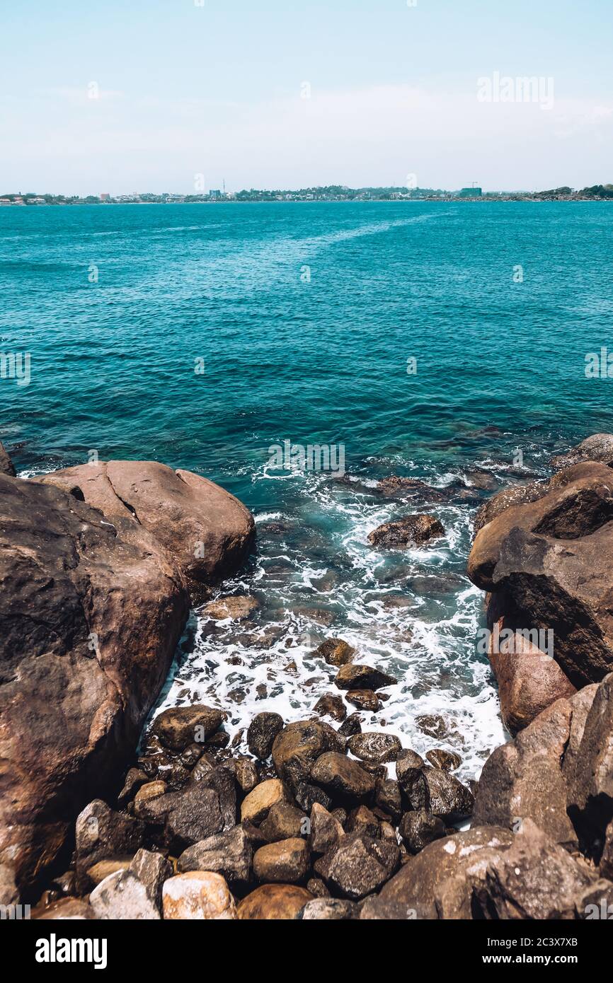 Wunderschöne blaue Wellen brechen auf Felsen und Kieselsteinen in der Nähe des Jungle Beach. Schöne Wasserfarbe, raues Meer und Horizont. Ruhiger Ort ohne Touristen Stockfoto