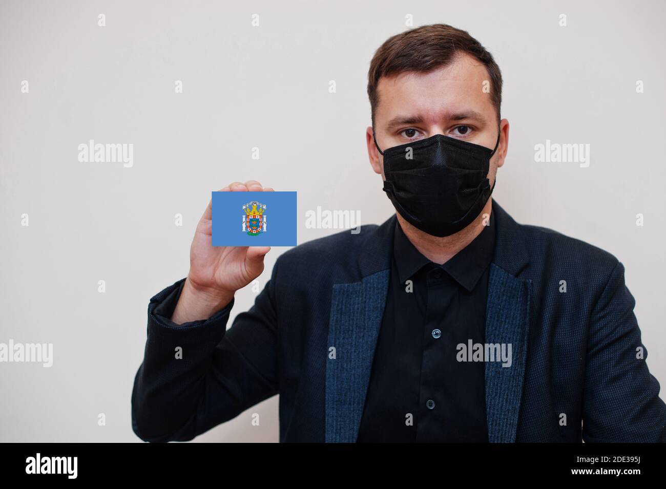 Spanisch Mann tragen schwarz formell und schützen Gesichtsmaske, halten Melilla Flagge Karte isoliert auf weißem Hintergrund. Spanien autonome Gemeinschaften Coronavirus Cov Stockfoto