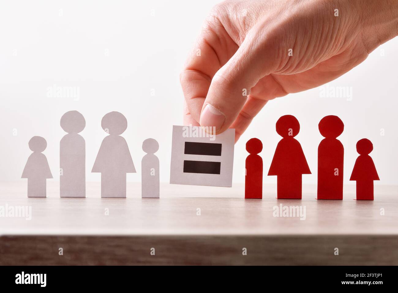 Gleichheit zwischen kultureller Vielfalt und Hand halten Zeichen mit gleichen Zeichen zwischen zwei Papierausschnitten mit der Form einer Person auf Holztisch. Stockfoto