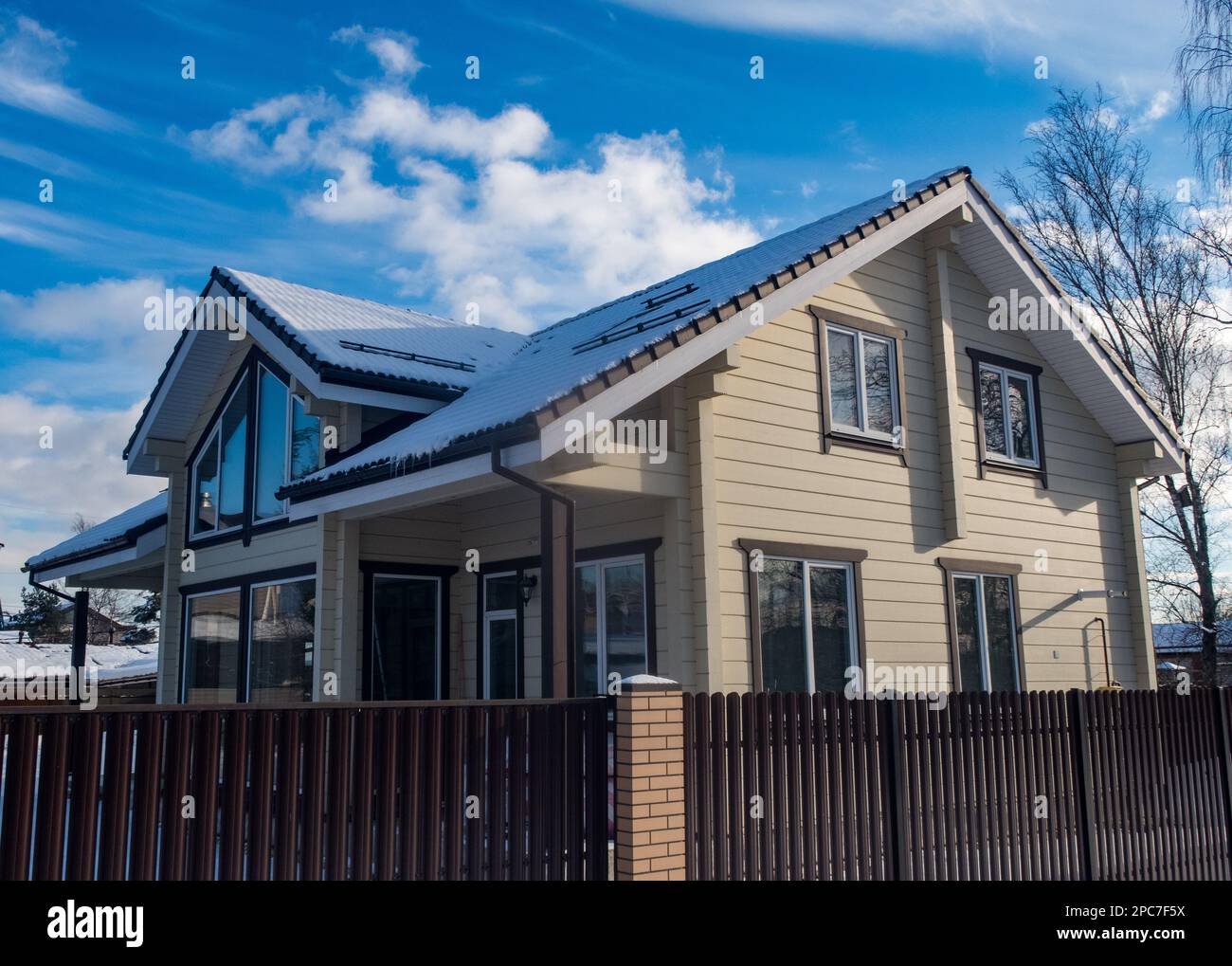 Ein zweistöckiges Haus, das mit großen Fenstern und einem Holzzaun vor einem blauen Himmel dekoriert ist Stockfoto