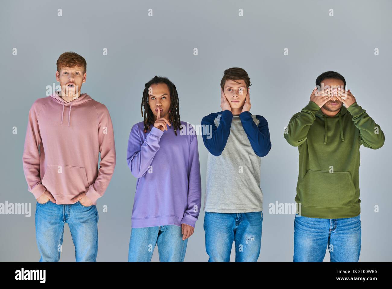 Vier Freunde in lässiger, heller Kleidung stehen und Gesten auf grauem Hintergrund, kulturelle Vielfalt Stockfoto